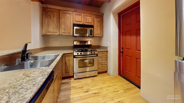 kitchen featuring light stone counters, light wood-style flooring, a sink, appliances with stainless steel finishes, and brown cabinetry