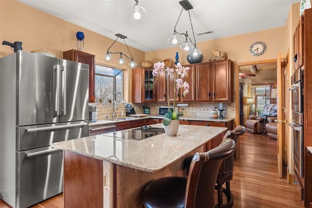 kitchen with light wood finished floors, decorative backsplash, a center island, stainless steel appliances, and a sink