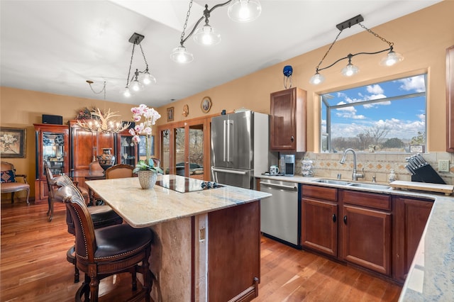 kitchen with a center island, stainless steel appliances, tasteful backsplash, a sink, and light wood-type flooring