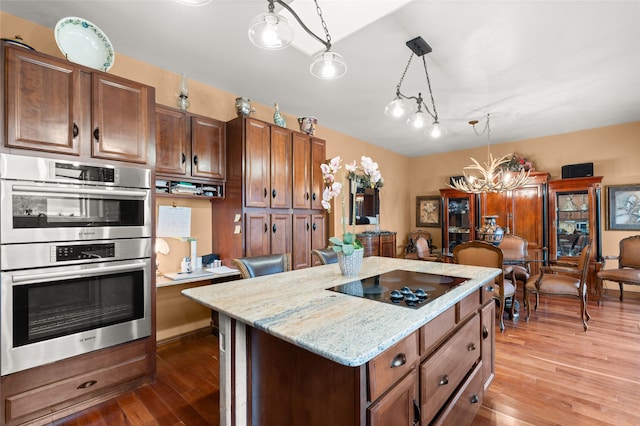 kitchen featuring double oven, black electric stovetop, hanging light fixtures, a center island, and dark wood finished floors