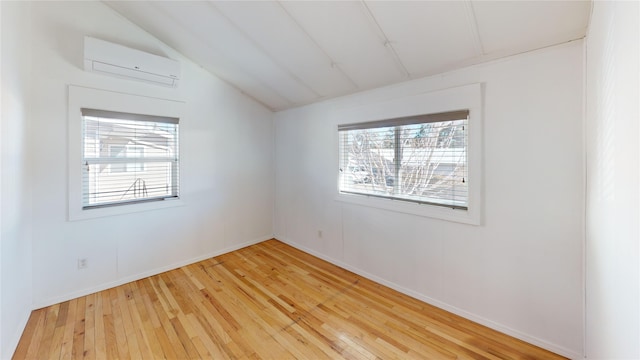 spare room featuring lofted ceiling, an AC wall unit, light wood finished floors, and baseboards