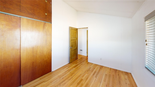 unfurnished bedroom featuring vaulted ceiling, a closet, light wood-style flooring, and baseboards