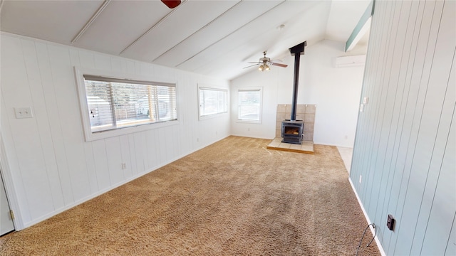 unfurnished living room with a ceiling fan, a wood stove, carpet, vaulted ceiling, and an AC wall unit