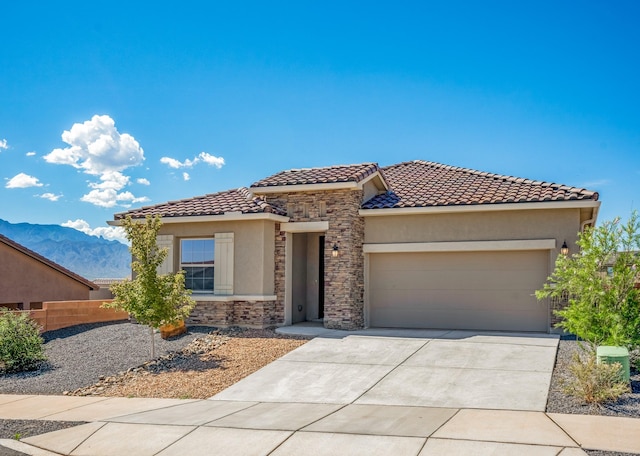 mediterranean / spanish house featuring a garage, stone siding, a tiled roof, driveway, and stucco siding