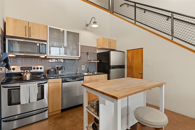 kitchen with stainless steel appliances, a high ceiling, a sink, wooden counters, and backsplash