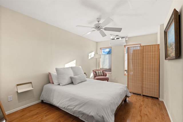 bedroom with light wood-style floors, a wall unit AC, ceiling fan, and baseboards