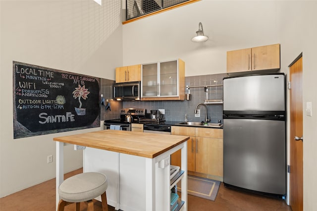 kitchen with decorative backsplash, a towering ceiling, butcher block counters, stainless steel appliances, and a sink