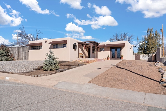 pueblo revival-style home with concrete driveway, french doors, fence, and stucco siding