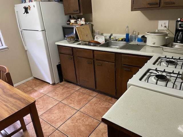 kitchen with light tile patterned floors, white appliances, a sink, light countertops, and dark brown cabinets