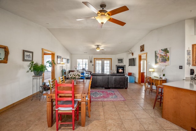 dining area featuring light tile patterned floors, baseboards, a ceiling fan, a glass covered fireplace, and vaulted ceiling