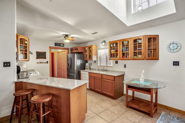 kitchen featuring a breakfast bar area, brown cabinetry, a sink, stainless steel fridge, and dishwasher