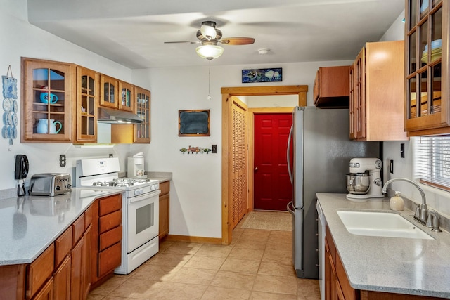 kitchen featuring brown cabinetry, glass insert cabinets, a sink, under cabinet range hood, and white gas range oven