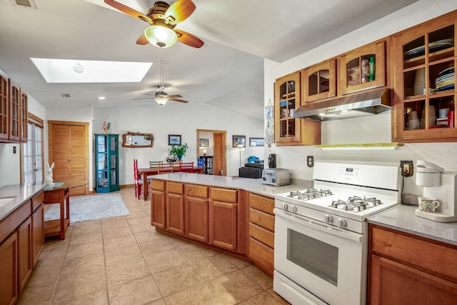 kitchen with brown cabinets, gas range gas stove, lofted ceiling with skylight, a peninsula, and under cabinet range hood