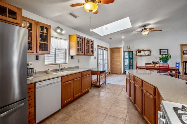 kitchen featuring visible vents, brown cabinetry, freestanding refrigerator, white dishwasher, and a sink