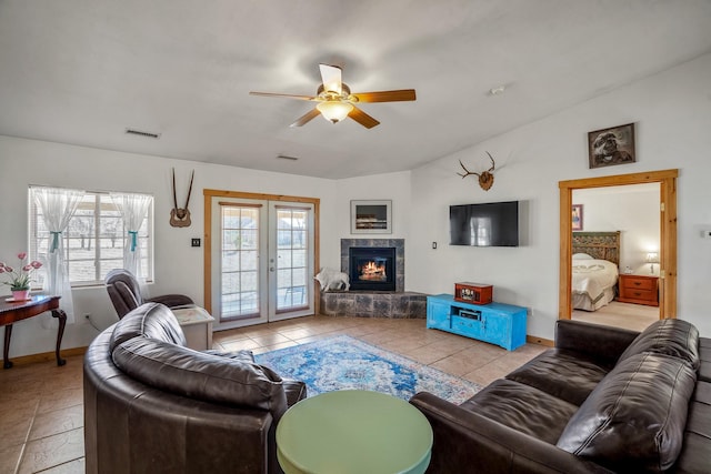 living area with visible vents, french doors, ceiling fan, vaulted ceiling, and a stone fireplace