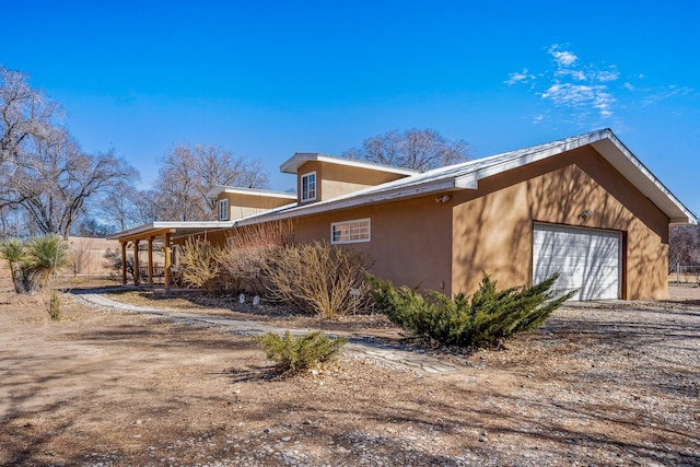 view of home's exterior with a garage, dirt driveway, and stucco siding