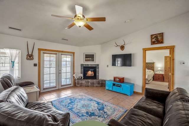 tiled living room with french doors, visible vents, a ceiling fan, a glass covered fireplace, and vaulted ceiling