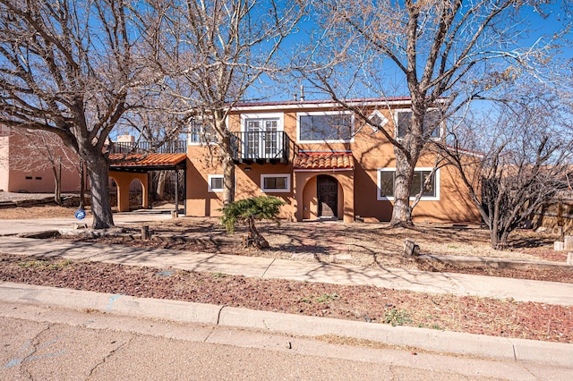 view of front of property featuring driveway, a balcony, a tile roof, and stucco siding