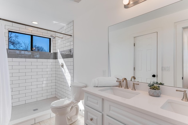 full bath with double vanity, tiled shower, a sink, and toilet