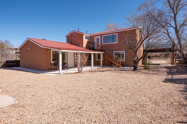 rear view of property with stucco siding, stairway, a patio area, metal roof, and a wooden deck