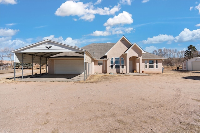 view of front of property with driveway, roof with shingles, a storage unit, and stucco siding