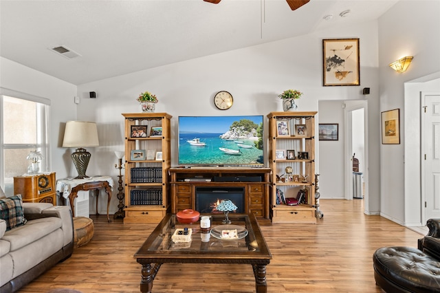 living area featuring light wood-style floors, lofted ceiling, a warm lit fireplace, and visible vents