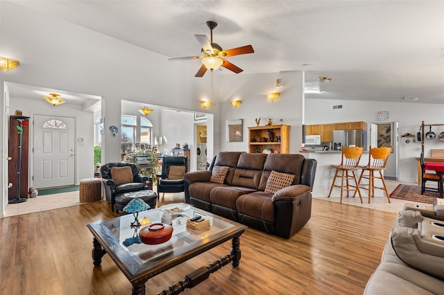 living room featuring a ceiling fan, visible vents, high vaulted ceiling, and light wood-style flooring