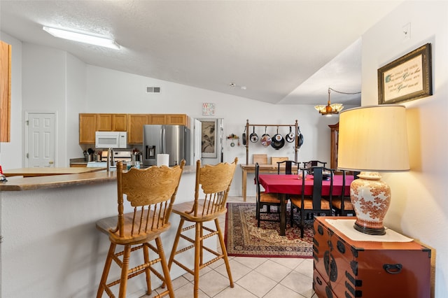 kitchen featuring white microwave, a breakfast bar area, stove, vaulted ceiling, and stainless steel fridge