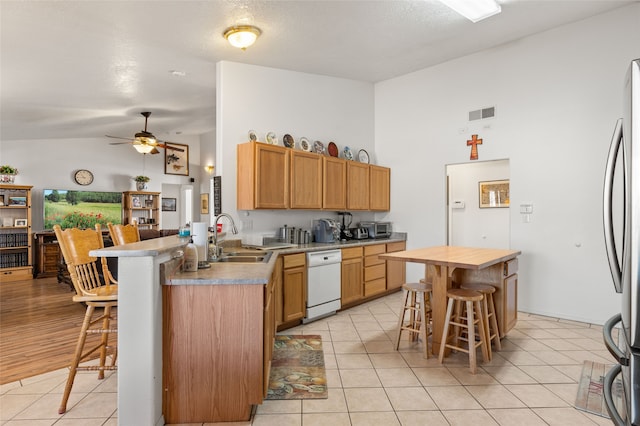 kitchen featuring light tile patterned floors, white dishwasher, a sink, and a kitchen breakfast bar