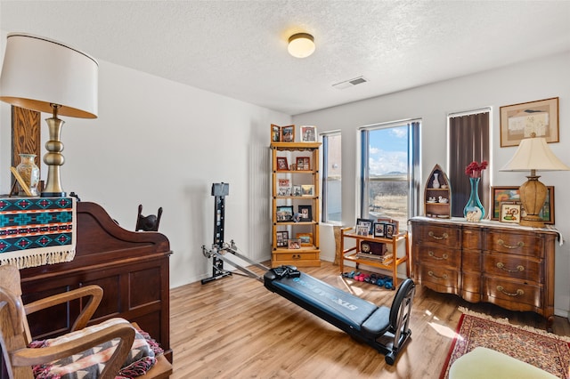 interior space featuring baseboards, a textured ceiling, visible vents, and wood finished floors