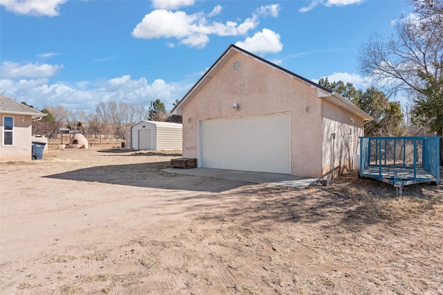 view of side of property featuring a shed, an outdoor structure, a detached garage, and stucco siding