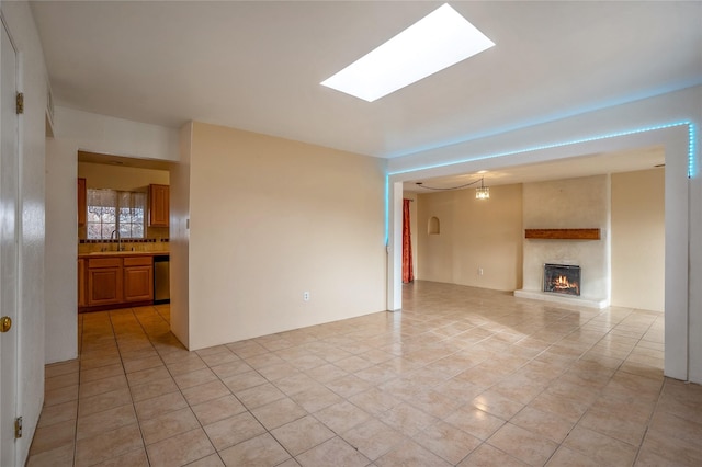 unfurnished living room featuring light tile patterned floors, a lit fireplace, a skylight, and a sink