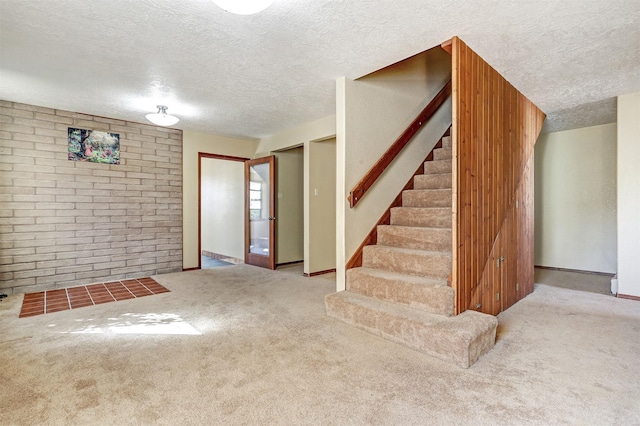 finished basement with baseboards, brick wall, stairs, a textured ceiling, and carpet flooring