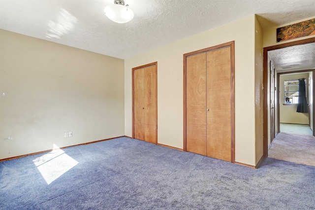 unfurnished bedroom with multiple closets, carpet flooring, a textured ceiling, and baseboards