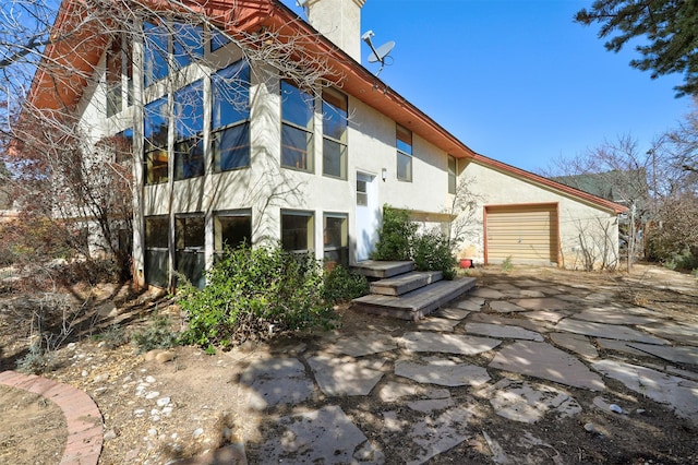 rear view of house with a garage, a chimney, and stucco siding