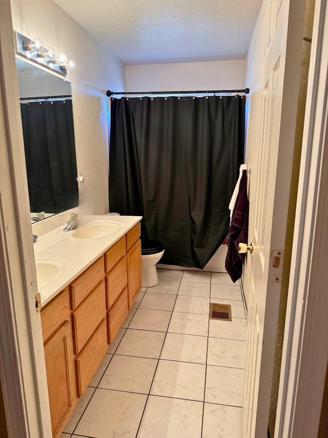 full bathroom featuring a textured ceiling, toilet, a sink, tile patterned floors, and double vanity