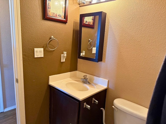 bathroom featuring a textured wall, vanity, and toilet