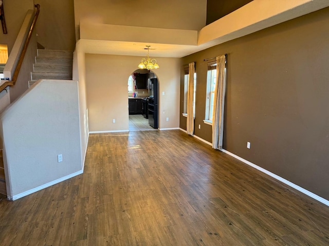 spare room featuring arched walkways, a notable chandelier, dark wood-type flooring, baseboards, and stairs