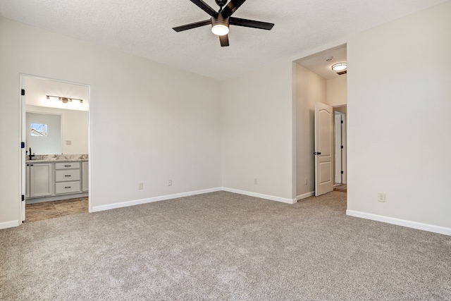 unfurnished bedroom featuring a textured ceiling, baseboards, connected bathroom, and light colored carpet