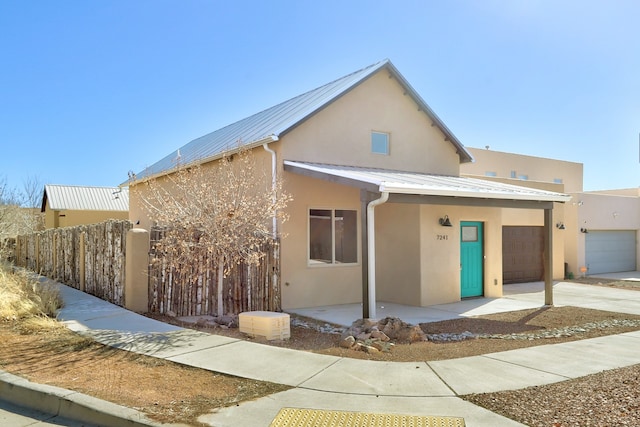 view of front of house featuring driveway, fence, metal roof, and stucco siding