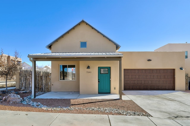 adobe home with driveway, metal roof, an attached garage, fence, and stucco siding