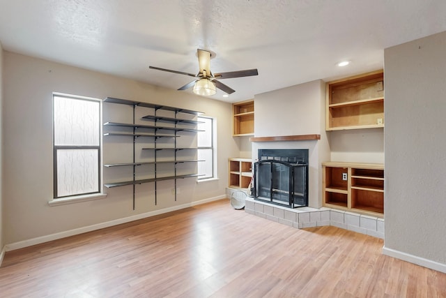 unfurnished living room featuring a fireplace, wood finished floors, a ceiling fan, and baseboards