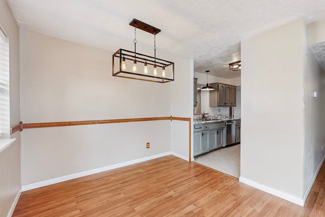 unfurnished dining area featuring a textured ceiling, a sink, light wood-style flooring, and baseboards