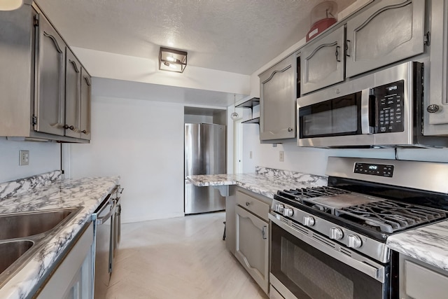 kitchen with stainless steel appliances, a sink, a textured ceiling, and gray cabinetry