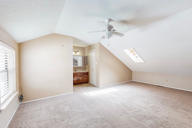 additional living space featuring vaulted ceiling with skylight, light carpet, plenty of natural light, and a textured ceiling