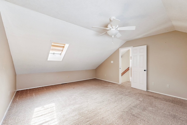 additional living space featuring lofted ceiling with skylight, carpet floors, baseboards, and a ceiling fan