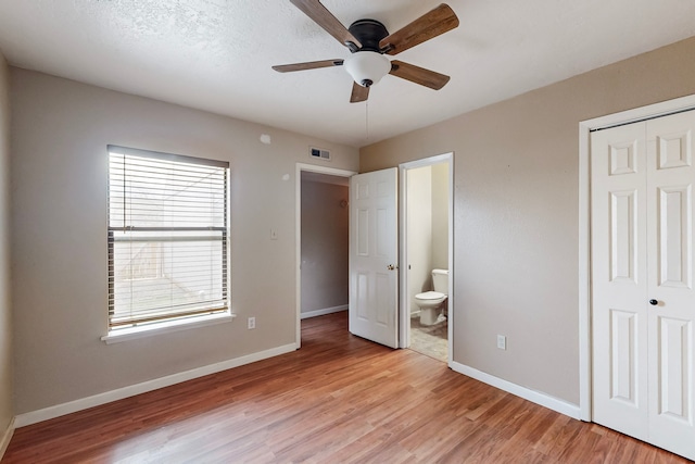 unfurnished bedroom featuring connected bathroom, light wood-style flooring, visible vents, baseboards, and a closet