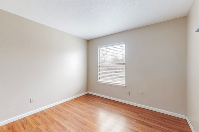 spare room featuring light wood-type flooring, baseboards, and a textured ceiling