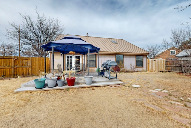 rear view of property with metal roof, french doors, and a fenced backyard