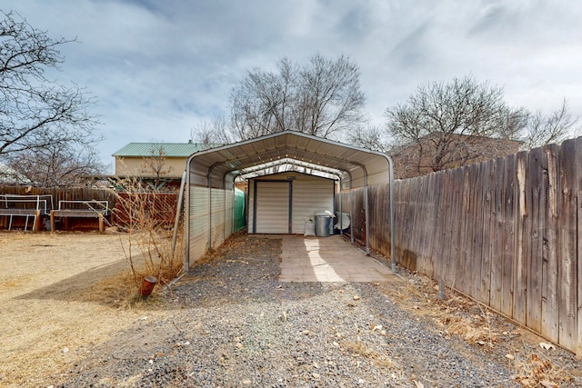 view of outdoor structure with driveway, a carport, and fence